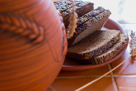 Sliced rye bread on a carved wooden board close-up. Against the background of pottery. Daylight. The kitchen table is covered with brown ceramic tiles.の写真素材