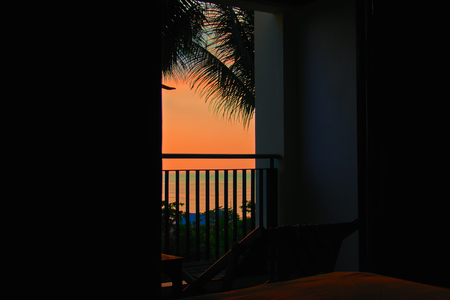 Late evening landscape in the tropics. View of the dark room at the orange sunset over the sea. Silhouettes of the leaves of palm trees. Copy space.の写真素材