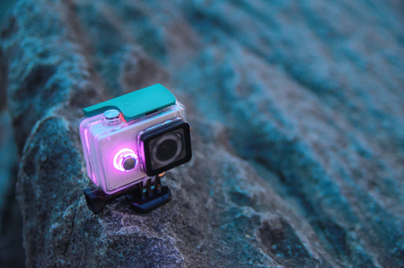 Action camera stands on a rock. Video camera in waterproof protective box with luminous diode indicators. Tourist gadget. Front view. Copy space.の写真素材