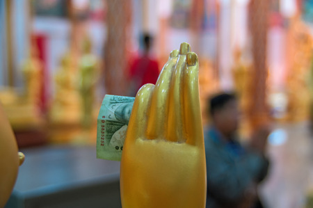 In the hand of the wax statue of a Buddhist monk inserted donation banknote. Concept of religious donations alms in Buddhist templeの写真素材