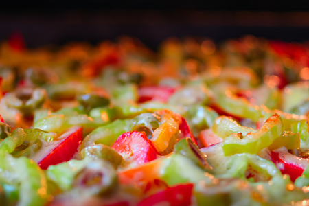 Pizza with sweet pepper, meat, vegetables, melted cheese, tomato and green olives on baking sheet. Selective focus, close-up. Dark oven background, side view. Copy space.の写真素材