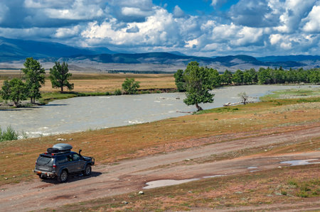 Mountain summer landscape. Steppe, river, tourist expedition car driving on a dirt road on the...