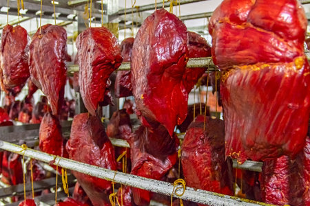 Large chunks of red meat hang in rows in the smokehouse. Juicy smoked meat, delicious food snack....