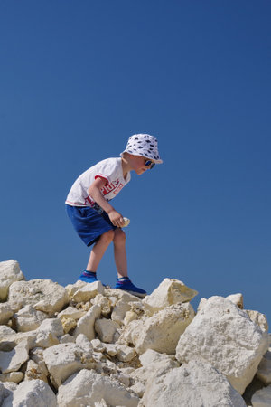 Russia, Moscow region, 10.07.2021 - Boy are looking for fossils. Hobby is paleontology. Walks on pile of limestone stones against the background of a blue sky, sunny summer day.のeditorial素材