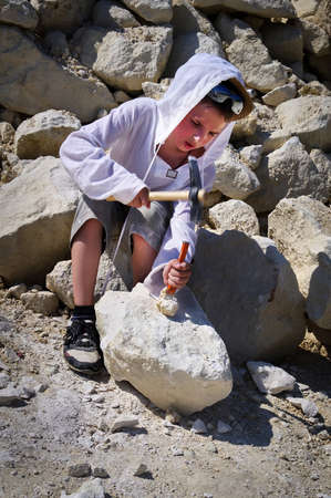 Boy are looking for fossils in a pile of limestone stones. Boy knocks a hammer on a stoneの写真素材