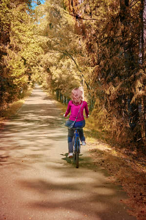 A girl on bicycle rides through sunny autumn park. Rear view.の写真素材