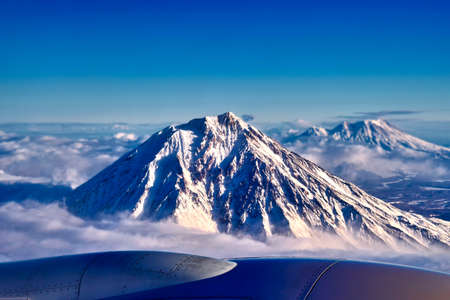 View of the snow-capped volcano from the aircraft's illuminator. Peak dormant volcano above the...