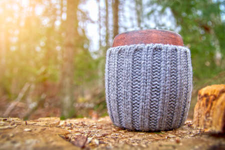 Clay mug in woolen cover stands in the autumn foliage in sunny beautiful forest. Background of green mossの写真素材