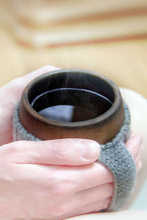 Cozy morning in bed with glanny mug of coffee, womens hands hold a mug in knitted cover. Close-up.の写真素材