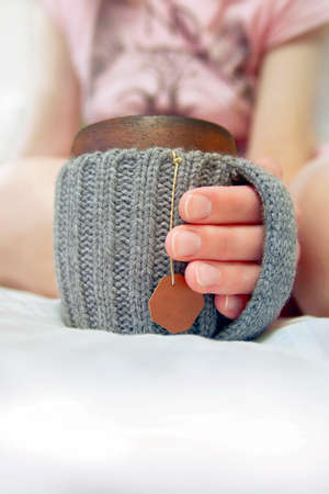 Cozy morning in bed with glanny mug of coffee, womens hands hold a mug in knitted cover. Close-up.の写真素材
