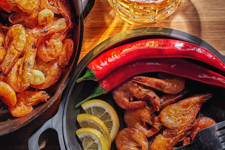 Big mug of beer, skillet of fried shrimp with pepper and lemonの写真素材