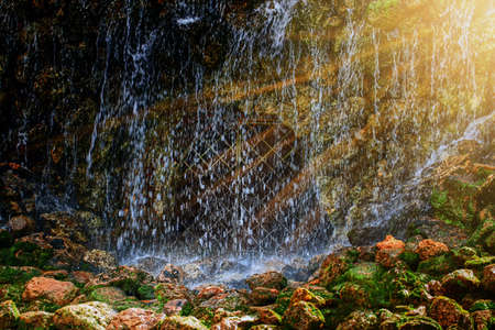 A large waterfall in a cave in the sun's raysの写真素材