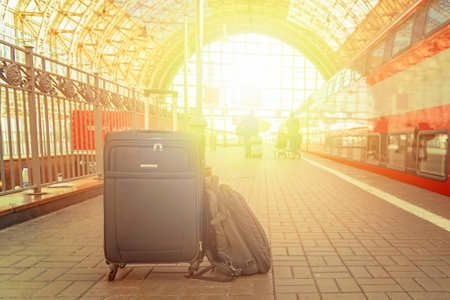 A suitcase and backpack stand on the platform of the railway station in the rays of the rising sun. Travel concept.の写真素材