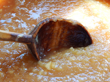 apple jam is brewed in a bowl and is stirred with a wooden spoon.の写真素材