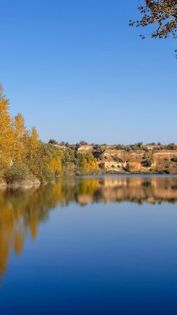 landscape river bank with yellow green trees on a summer day reflected in waterの写真素材