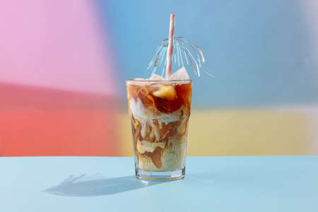 A glass of ice coffee with a straw on a colored background.の写真素材