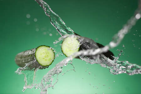 Fresh cucumber slices with water splash on green background, closeupの写真素材