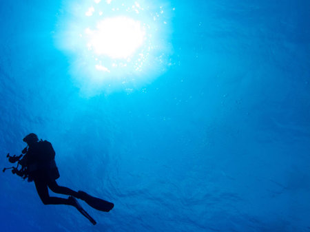 Silhouetted diver with blue water background and sun ballの写真素材
