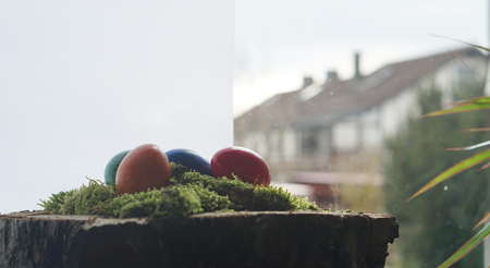 at home Easter wooden block with green moos and colorful easter eggs front of window and blurred houseの写真素材