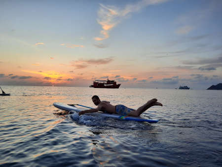 on a stand up paddle board, young man 34 years old, German, lies on a board on the ocean in Thailand, on the island Koh Tao at sunsetの写真素材