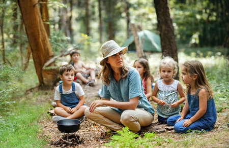 kindergarten teacher and the group of kids, they make an outdoor nature trip in the forest and are cooking something together, young kids childrenの素材