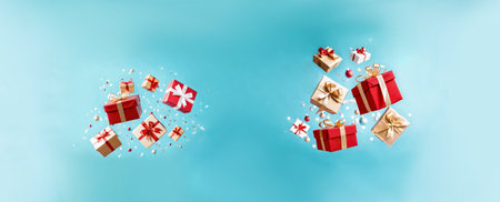 festive red and gold gift boxes with shiny bows floating mid-air with confetti and ornaments against a bright blue panoramic backgroundの素材