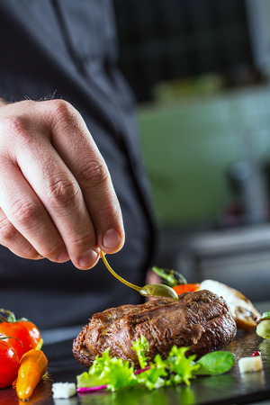 Chef in hotel or restaurant kitchen cooking only hands. Prepared beef steak with vegetable decorationの写真素材