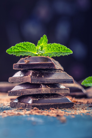 Chocolate. Black chocolate. A few cubes of black chocolate with mint leaves. Chocolate slabs spilled from grated chockolate powder.の写真素材