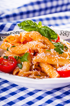 Plate with pasta pene Bolognese sauce cherry tomatoes parsley top and basil leaves on checkered blue tablecloth. Italian and Mediterranean cuisineの写真素材