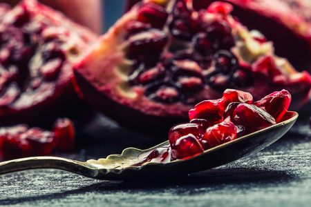 Pieces and grains of ripe pomegranate. Pomegranate seeds. Part of pomegranate fruit on granite board and antique spoon. Mediterranean fruit.の写真素材