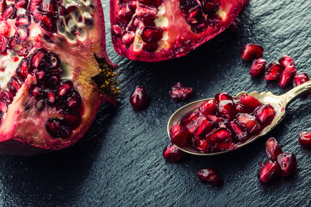 Pieces and grains of ripe pomegranate. Pomegranate seeds. Part of pomegranate fruit on granite board and antique spoon. Mediterranean fruit.の写真素材