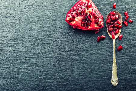 Pieces and grains of ripe pomegranate. Pomegranate seeds. Part of pomegranate fruit on granite board and antique spoon. Mediterranean fruit.の写真素材