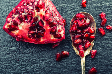 Pieces and grains of ripe pomegranate. Pomegranate seeds. Part of pomegranate fruit on granite board and antique spoon. Mediterranean fruit.の写真素材