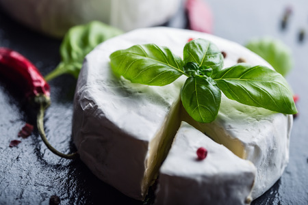 Brie cheese. Camembert cheese. Fresh Brie cheese and a slice on a granite board with basil leaves four colors peper and chili pepers. Italian and Mediterranean ingredients.の写真素材