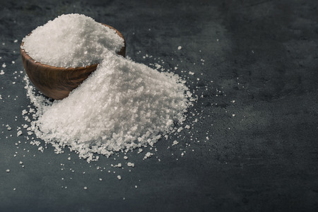 Salt. Coarse grained sea salt on granite - concrete  stone background with vintage spoon and wooden bowl.の写真素材