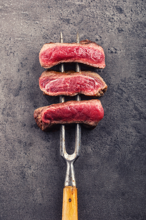 Slices of sirloin beef steak on meat fork on concrete background.の写真素材