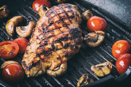 Grilled chicken breast in different variations with cherry tomatoes, mushrooms, herbs, cut lemon on a wooden board or teflon pan. Traditional cuisine. Grill kitchen.の写真素材