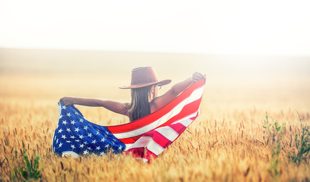 Pretty young pre-teen girl with an American cowboy hat in corn field and the holding American flag.の写真素材