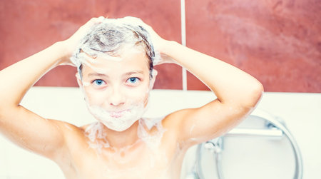 Cute young girl in shower washing hair and face with shampoo.