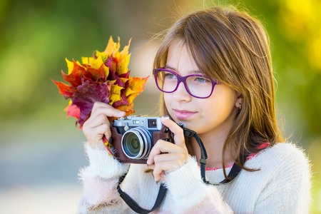 Autumn time. The teenage attractive cute young girl with autumn bouquet and retro camera. Young girl photographer autumn  season.の写真素材
