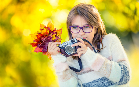 Autumn time. The teenage attractive cute young girl with autumn bouquet and retro camera. Young girl photographer autumn  season.の写真素材