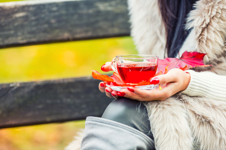Young attractive woman holding in hand hot red tea. Relaxing in autumn nature with hot tea.の写真素材