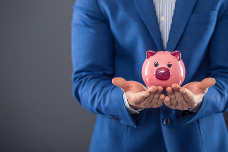 Saving money. Businesman holding pink piggy  and putting coin into piggy bank.の写真素材