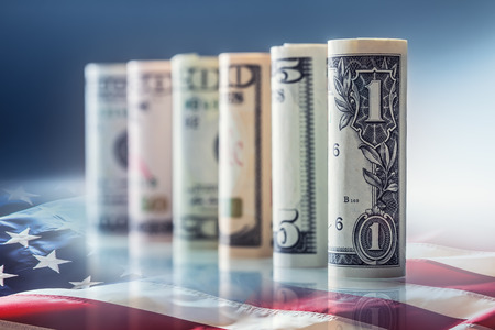 Dollar and American flag. American dollar banknotes rolled in different positions and USA flag in the background.の写真素材