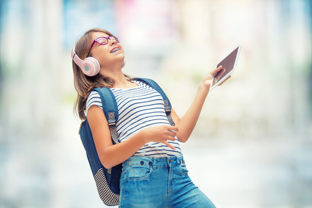 Schoolgirl with bag, backpack. Portrait of modern happy teen school girl with bag backpack headphones and tablet. Girl with dental braces and glasses.の写真素材