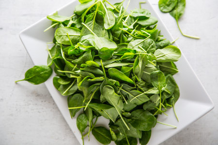 Top of view fresh spinach leaves in bowl on white concrete board.