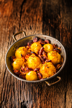 Potatoes. Roasted potatoes with bacon onion and sausages on old oak table.の写真素材