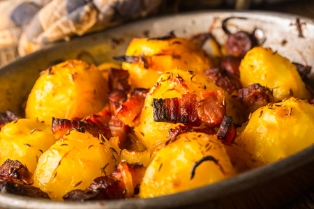Potatoes. Roasted potatoes with bacon onion and sausages on old oak table.の写真素材