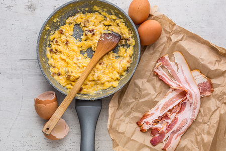 Ham and eggs. Scrambled eggs with bacon in ceramic pan.の写真素材
