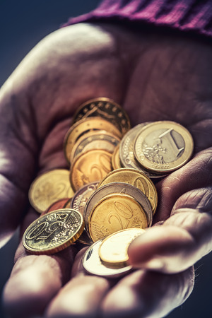Pensioner man holding in hands euro coins. Theme of low pensions.の写真素材